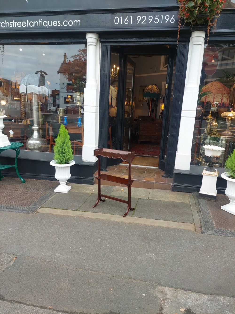 An Edwardian mahogany two-tier standing book trough featuring a shaped top apron, middle shelf, carved stretcher, and splayed legs. View II