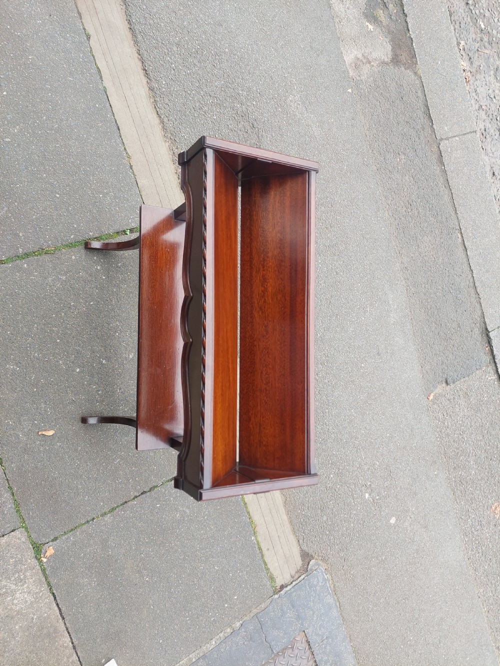 An Edwardian mahogany two-tier standing book trough featuring a shaped top apron, middle shelf, carved stretcher, and splayed legs. View III