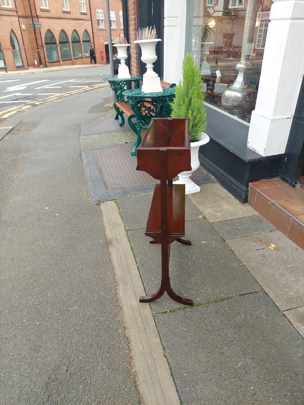 An Edwardian mahogany two-tier standing book trough featuring a shaped top apron, middle shelf, carved stretcher, and splayed legs. View V