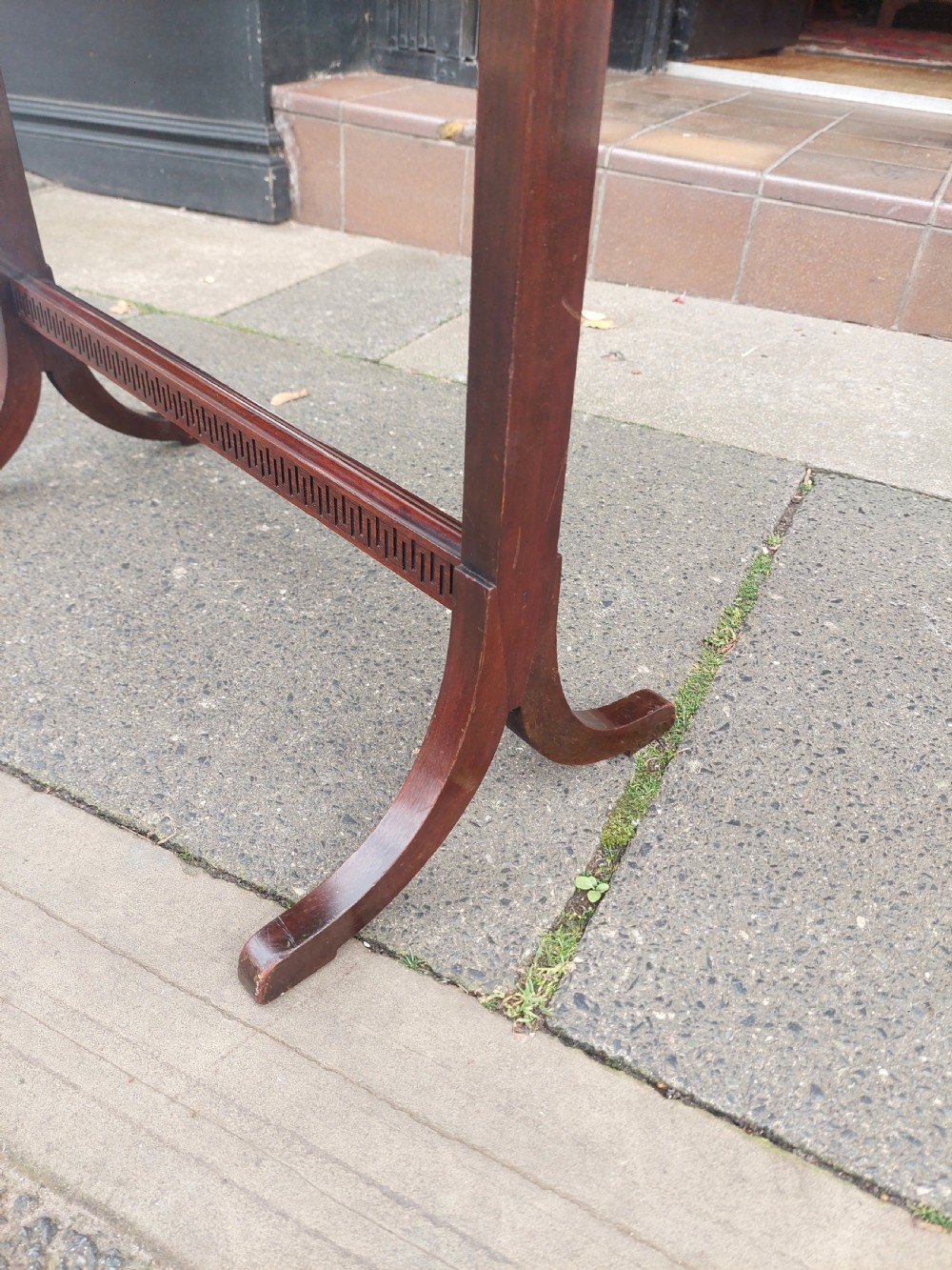 An Edwardian mahogany two-tier standing book trough featuring a shaped top apron, middle shelf, carved stretcher, and splayed legs. View VI