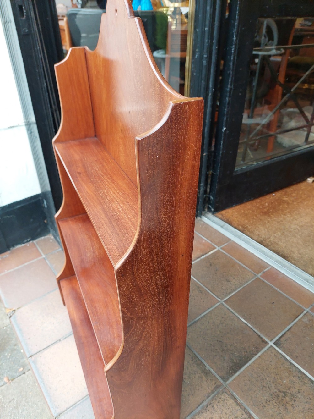 An Edwardian mahogany wall-hanging bookshelf featuring three open tiers, shaped side panels, an arched top cresting, and a polished warm brown finish. View VII