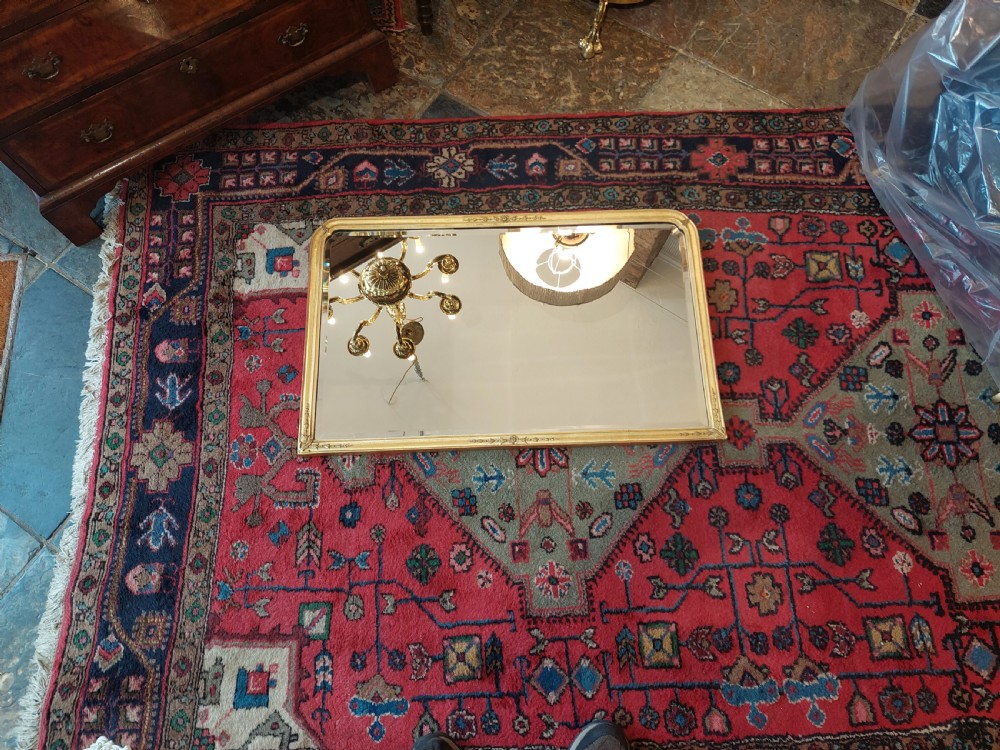 A 19th-century rectangular giltwood overmantel mirror with rounded top corners and subtle leaf moulding details along the gold frame. View II