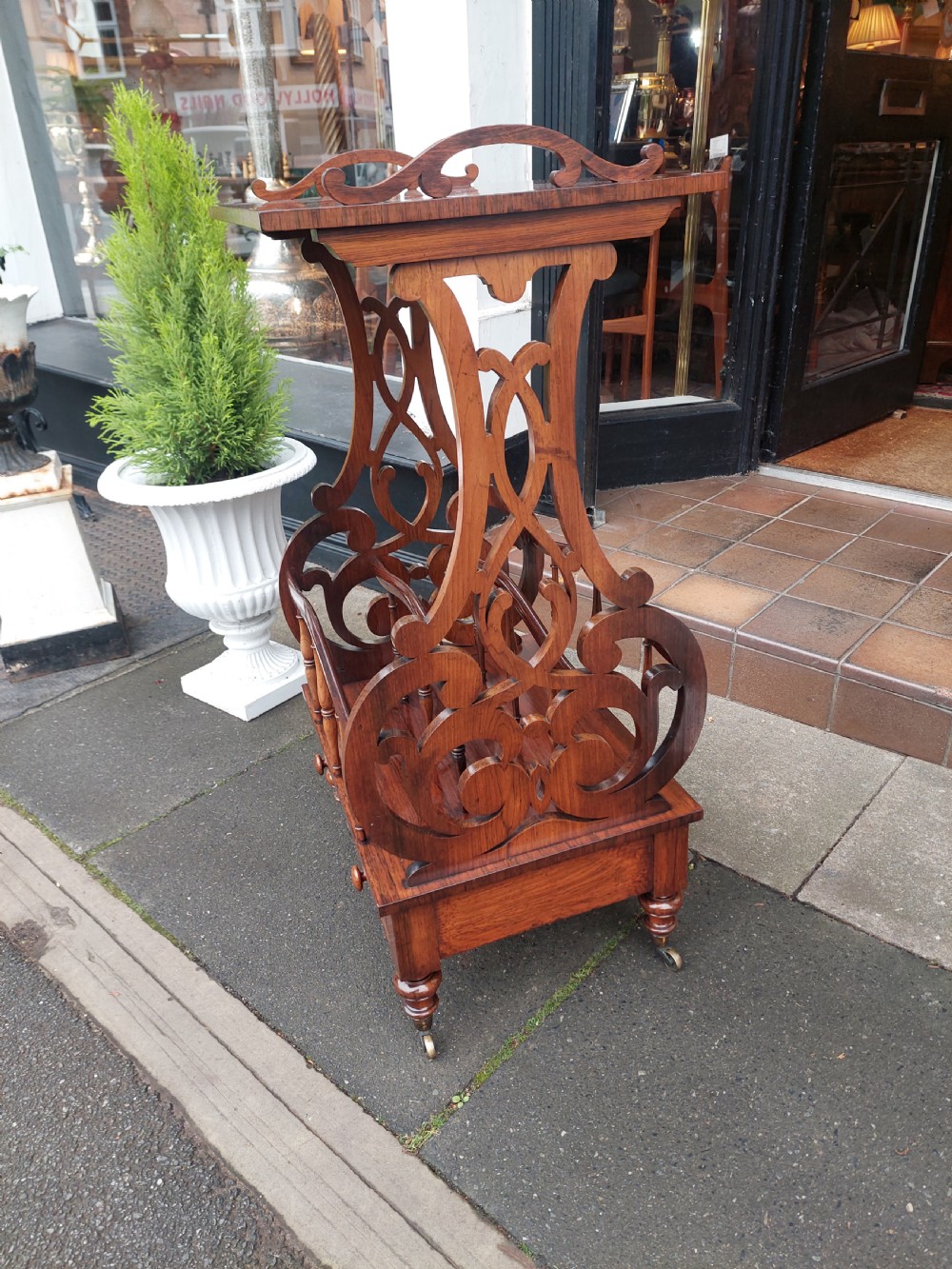 A Victorian rosewood Canterbury whatnot featuring a top shelf supported by pierced fretwork side panels, slatted sheet music partitions, a lower drawer, and turned legs with brass castors. View VI