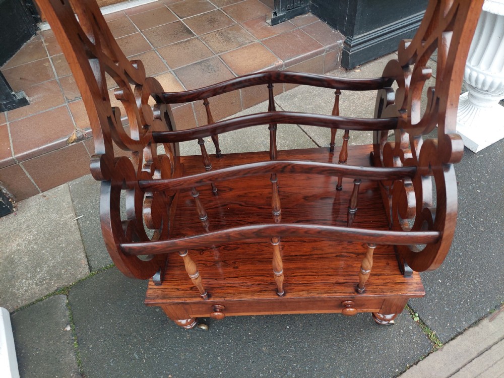 A Victorian rosewood Canterbury whatnot featuring a top shelf supported by pierced fretwork side panels, slatted sheet music partitions, a lower drawer, and turned legs with brass castors. View VIII