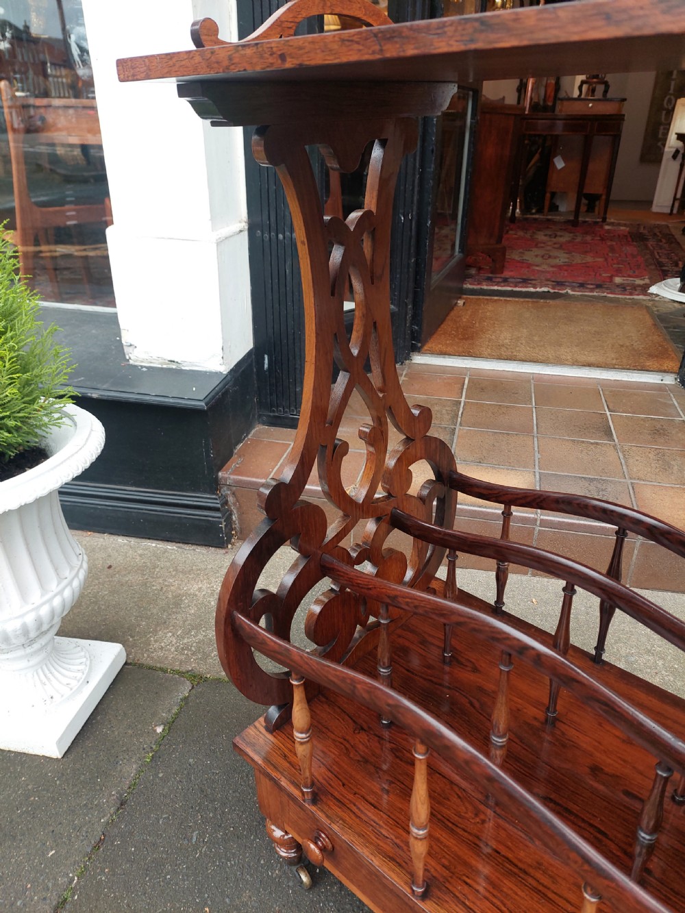 A Victorian rosewood Canterbury whatnot featuring a top shelf supported by pierced fretwork side panels, slatted sheet music partitions, a lower drawer, and turned legs with brass castors. View IX