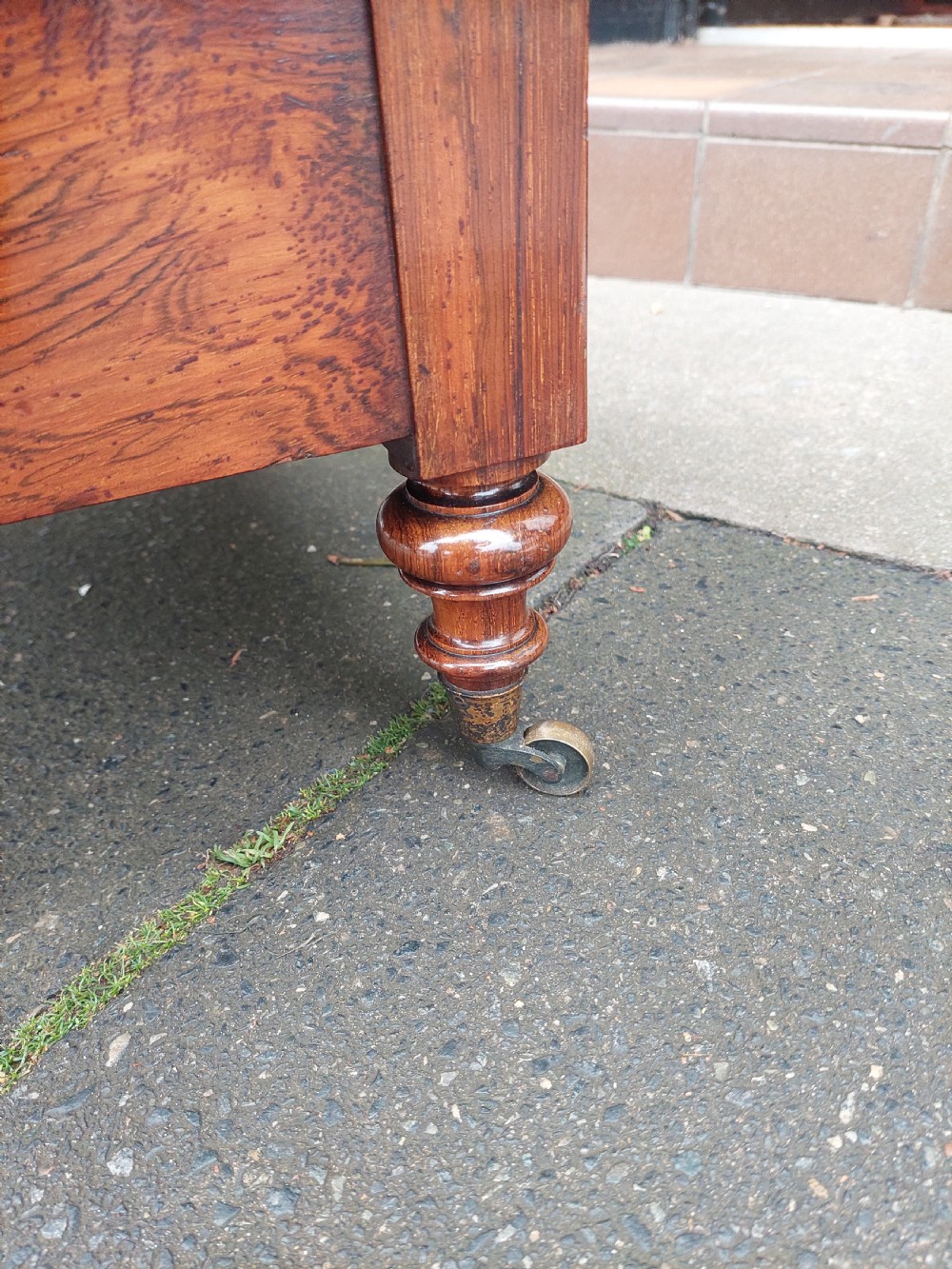A Victorian rosewood Canterbury whatnot featuring a top shelf supported by pierced fretwork side panels, slatted sheet music partitions, a lower drawer, and turned legs with brass castors. View X