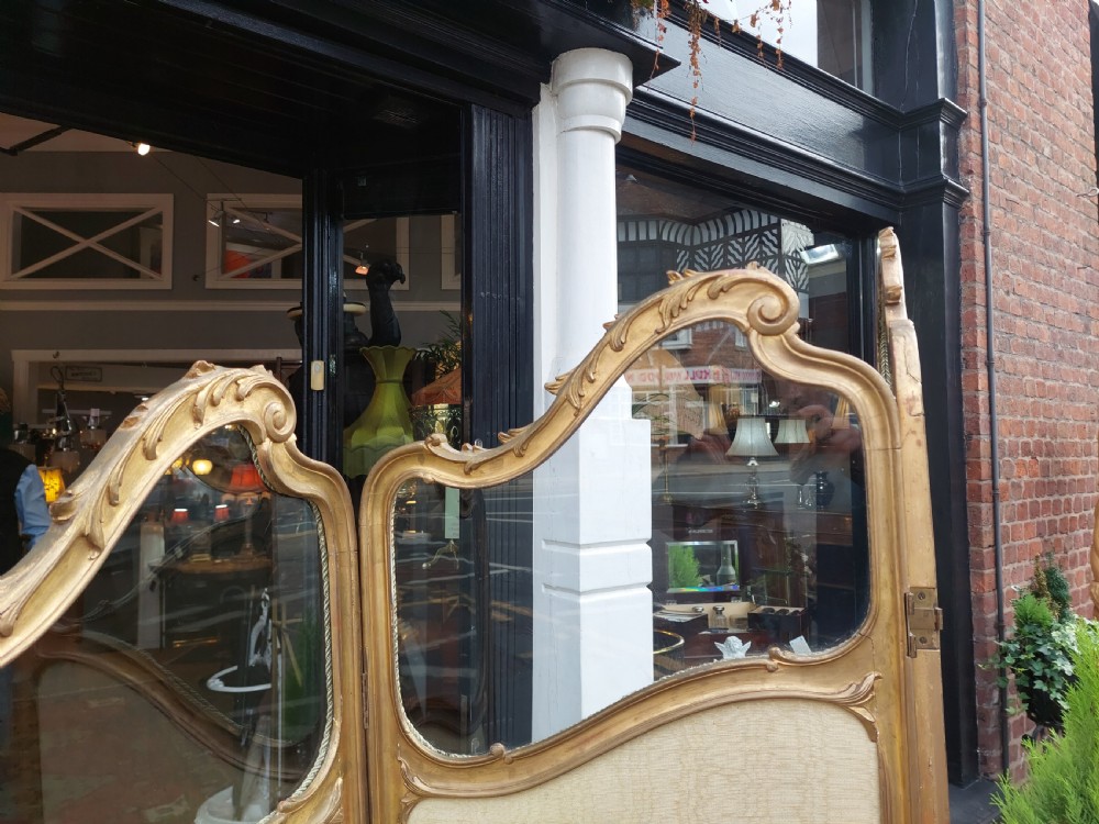 A mid-19th century three-panel giltwood vanity screen featuring carved Rococo cresting, clear glass top panels, and cream upholstered lower panels. View III