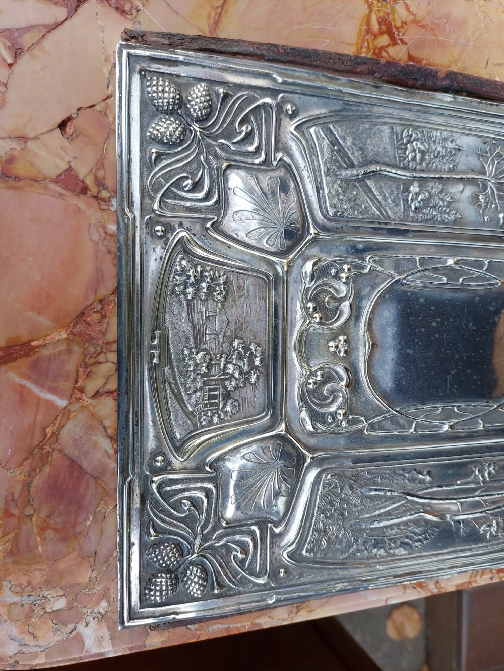 A rectangular silver-plated Art Nouveau blotter folio featuring relief embossed panels of trees, landscapes, pinecone motifs, and a central polished cartouche. View V