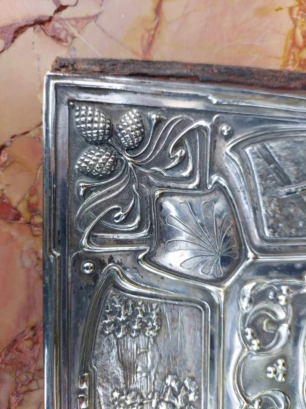 A rectangular silver-plated Art Nouveau blotter folio featuring relief embossed panels of trees, landscapes, pinecone motifs, and a central polished cartouche. View VI
