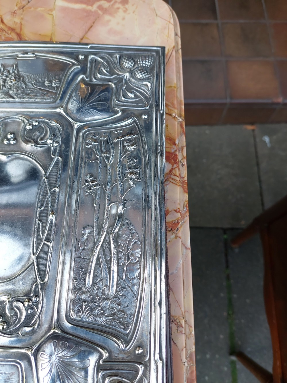 A rectangular silver-plated Art Nouveau blotter folio featuring relief embossed panels of trees, landscapes, pinecone motifs, and a central polished cartouche. View IX