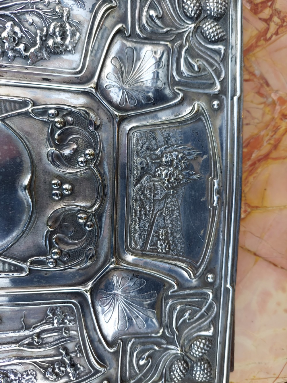 A rectangular silver-plated Art Nouveau blotter folio featuring relief embossed panels of trees, landscapes, pinecone motifs, and a central polished cartouche. View XI