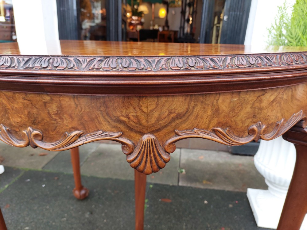 A semi-circular walnut fold-over card table with figured veneer top, carved apron, cabriole legs, and ball and claw feet. View II