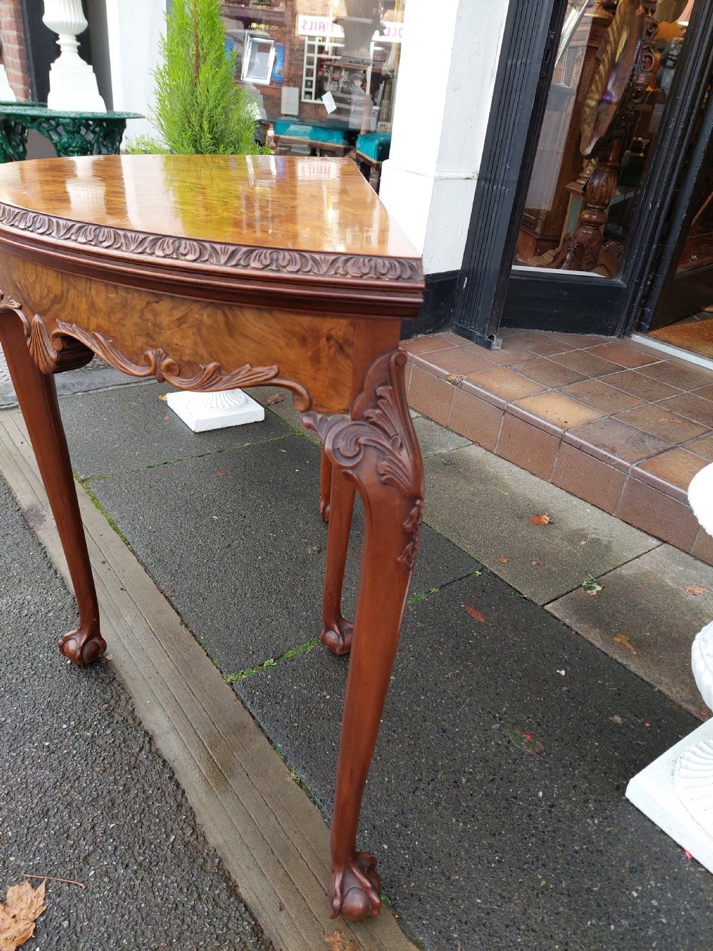 A semi-circular walnut fold-over card table with figured veneer top, carved apron, cabriole legs, and ball and claw feet. View III
