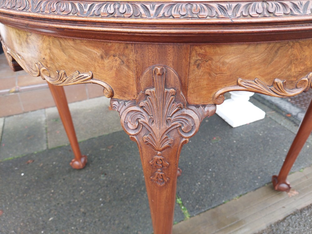 A semi-circular walnut fold-over card table with figured veneer top, carved apron, cabriole legs, and ball and claw feet. View IV