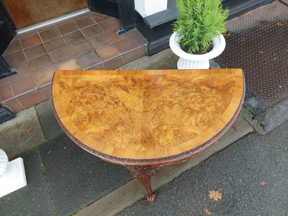 A semi-circular walnut fold-over card table with figured veneer top, carved apron, cabriole legs, and ball and claw feet. View VI