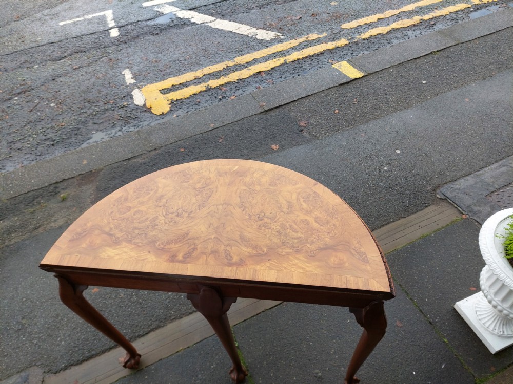 A semi-circular walnut fold-over card table with figured veneer top, carved apron, cabriole legs, and ball and claw feet. View VII