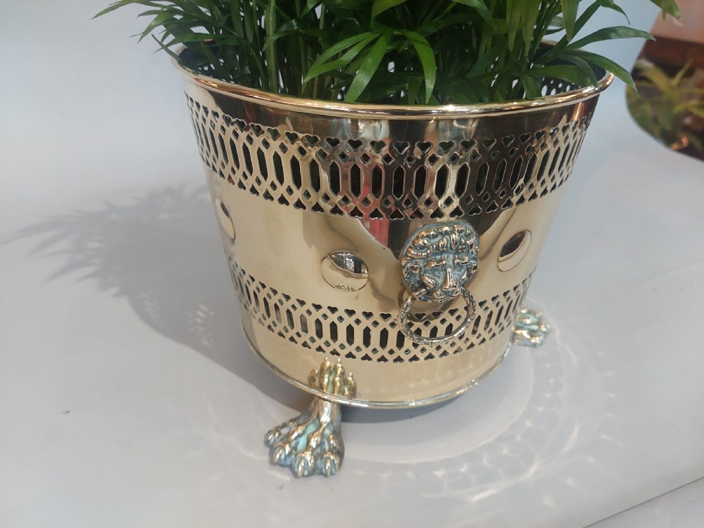 A cylindrical polished brass planter featuring pierced lattice bands, central circular bosses, side lion mask ring handles, and three claw feet. View III