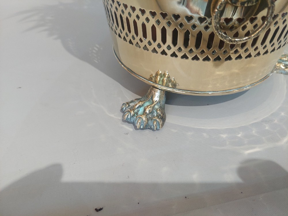 A cylindrical polished brass planter featuring pierced lattice bands, central circular bosses, side lion mask ring handles, and three claw feet. View IV