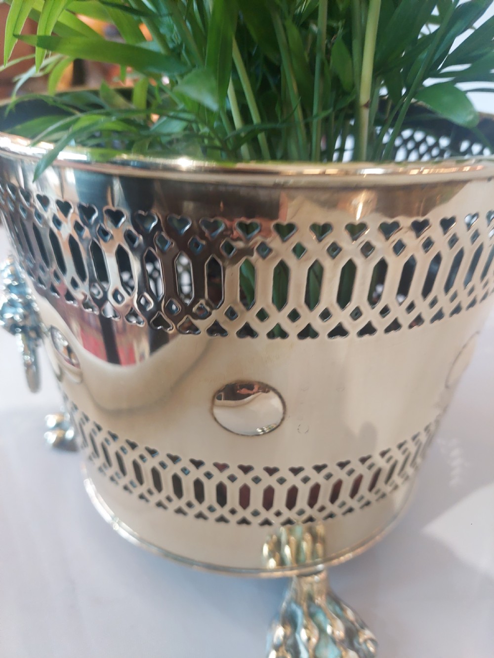 A cylindrical polished brass planter featuring pierced lattice bands, central circular bosses, side lion mask ring handles, and three claw feet. View VI