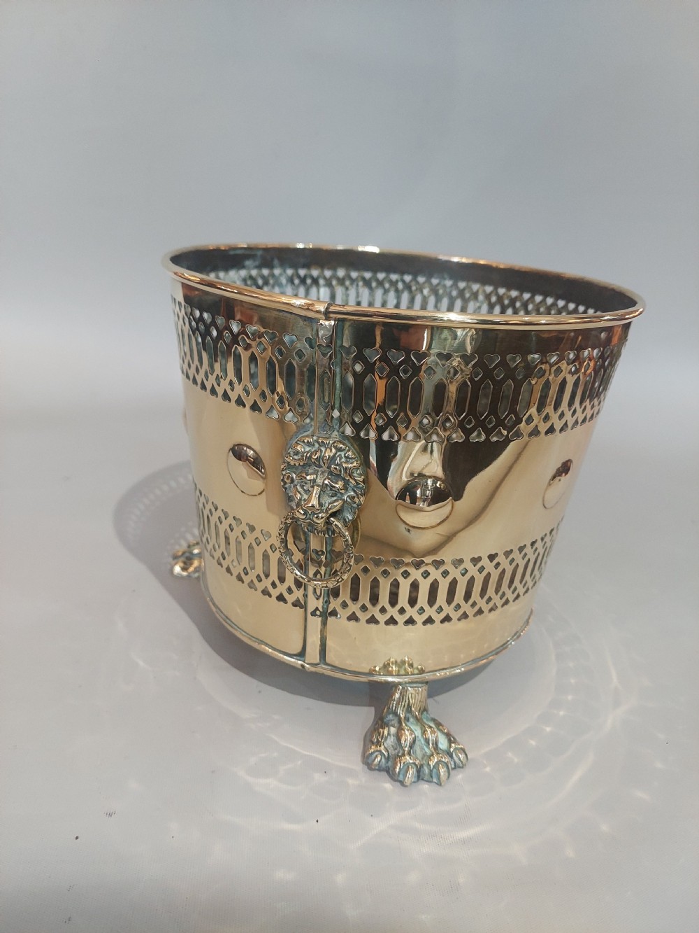A cylindrical polished brass planter featuring pierced lattice bands, central circular bosses, side lion mask ring handles, and three claw feet. View VII