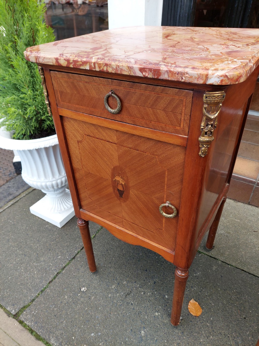 A pair of late nineteenth-century French walnut bedside cabinets featuring pink veined marble tops, marquetry floral inlay on the doors, brass mounts, and slender turned legs. View IV