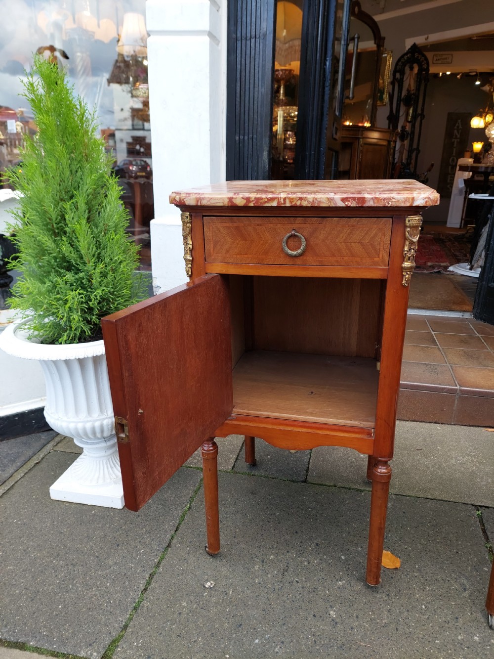 A pair of late nineteenth-century French walnut bedside cabinets featuring pink veined marble tops, marquetry floral inlay on the doors, brass mounts, and slender turned legs. View V