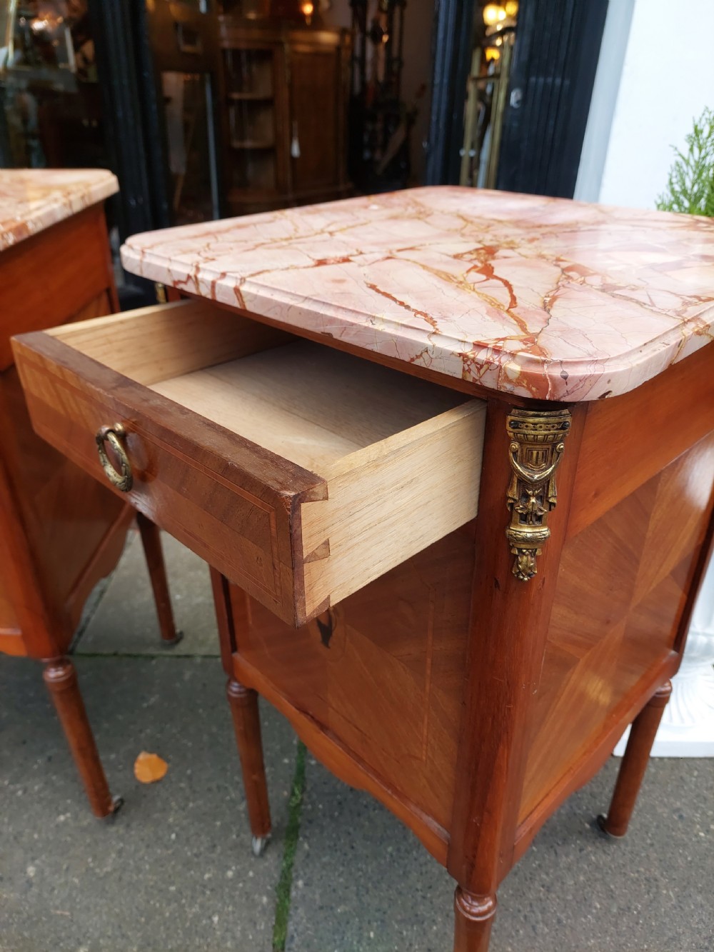 A pair of late nineteenth-century French walnut bedside cabinets featuring pink veined marble tops, marquetry floral inlay on the doors, brass mounts, and slender turned legs. View VI