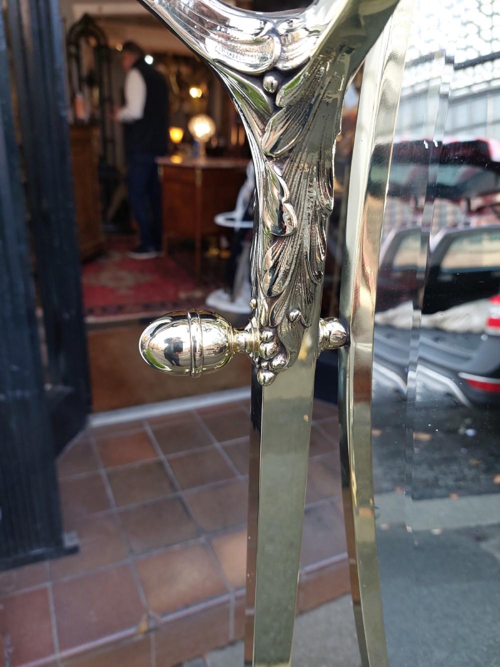 An Edwardian brass cheval mirror featuring an oval bevelled glass frame with decorative cresting and side candle sconces supported on a slender standing base. View III