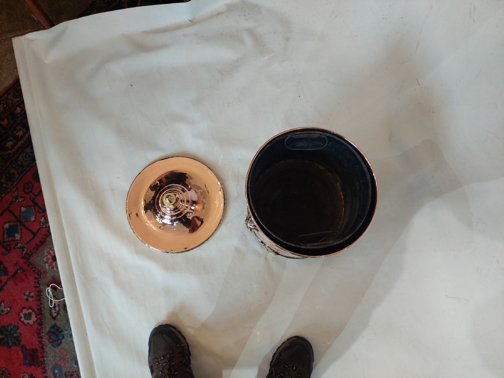A cylindrical polished copper coal bucket featuring a fitted lid with a brass finial, side ring handles attached to lion mask mounts, and four detailed brass paw feet. View V