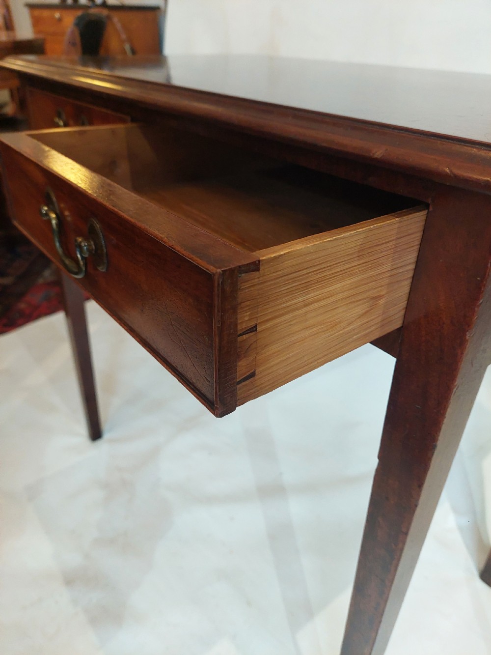 A mid-18th-century Georgian mahogany hall table featuring two drawer fronts with brass swan-neck handles and square tapered legs. View VI