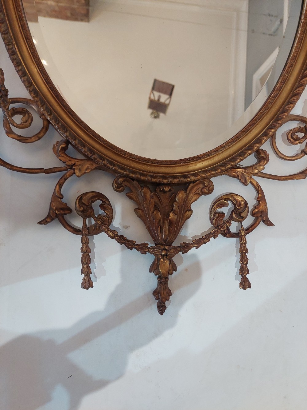 A late Victorian Adam Revival giltwood oval wall mirror decorated with an urn cresting, trailing ribbon swags, and scrollwork accents. View IV