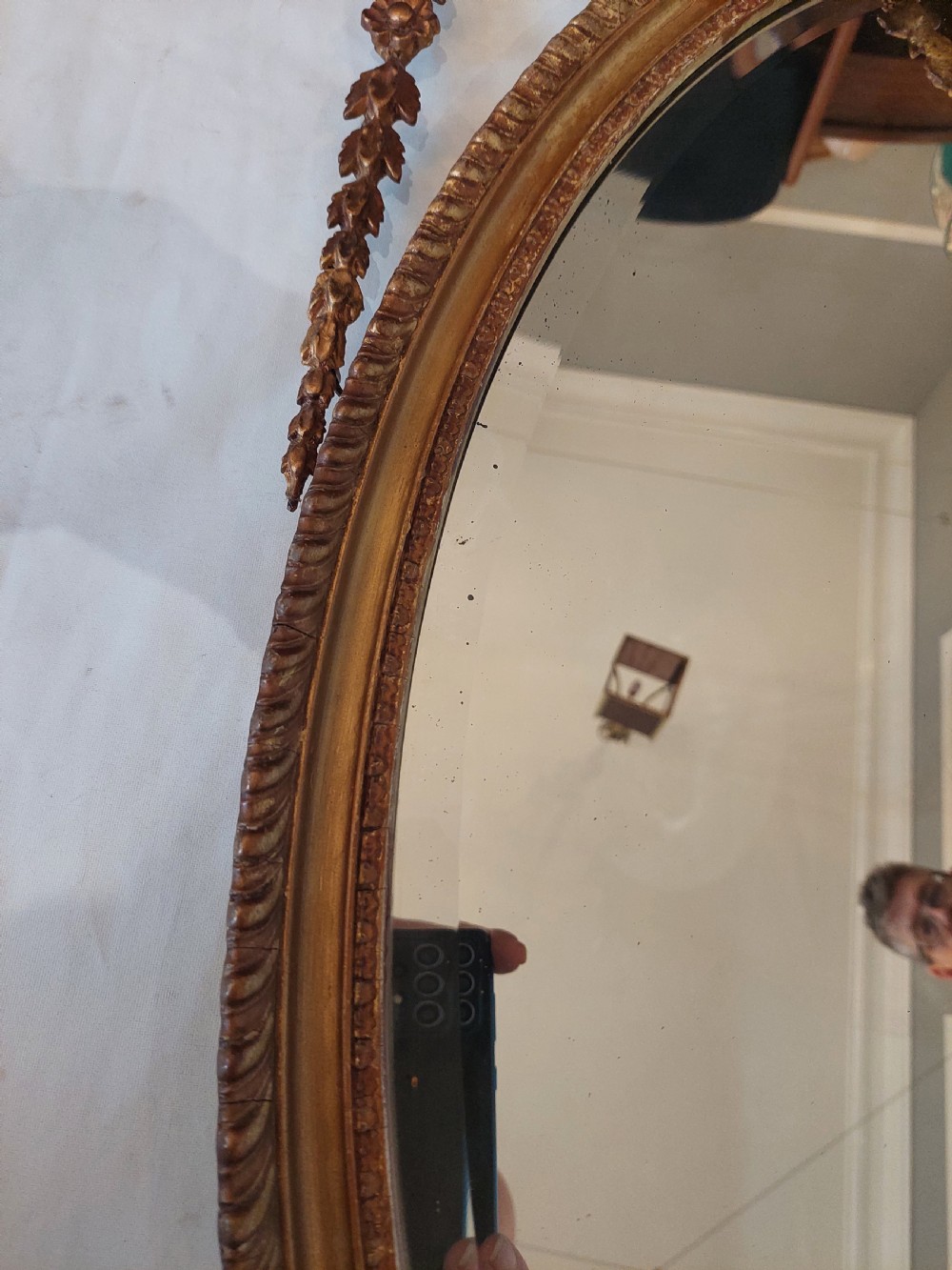 A late Victorian Adam Revival giltwood oval wall mirror decorated with an urn cresting, trailing ribbon swags, and scrollwork accents. View V
