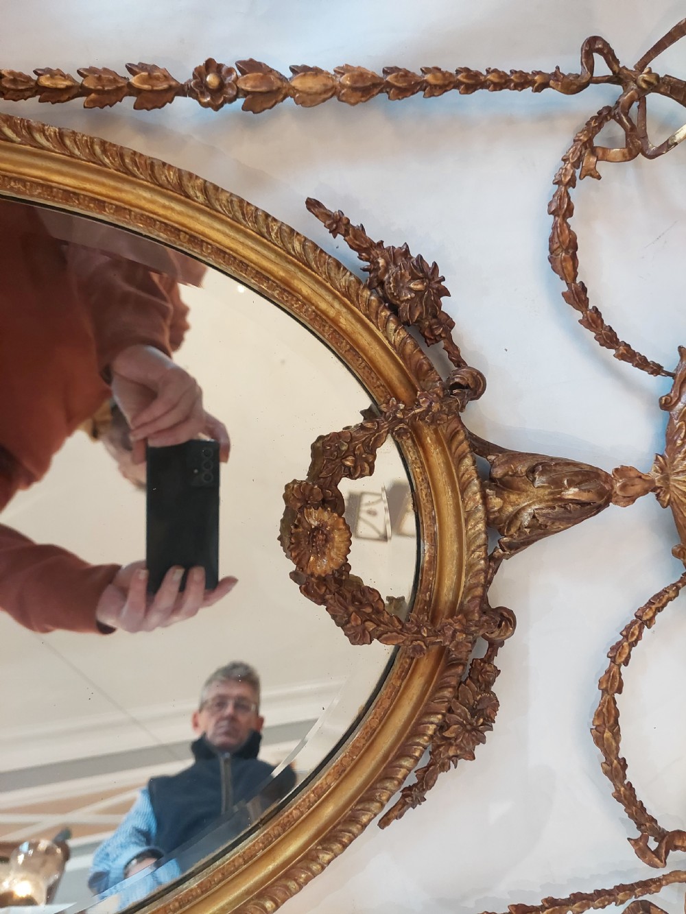 A late Victorian Adam Revival giltwood oval wall mirror decorated with an urn cresting, trailing ribbon swags, and scrollwork accents. View XI