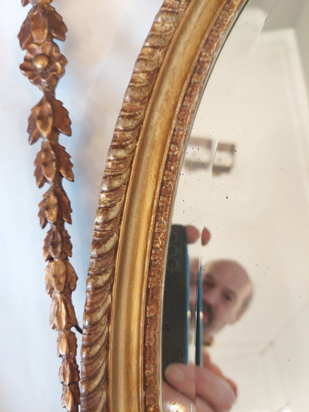 A late Victorian Adam Revival giltwood oval wall mirror decorated with an urn cresting, trailing ribbon swags, and scrollwork accents. View XII