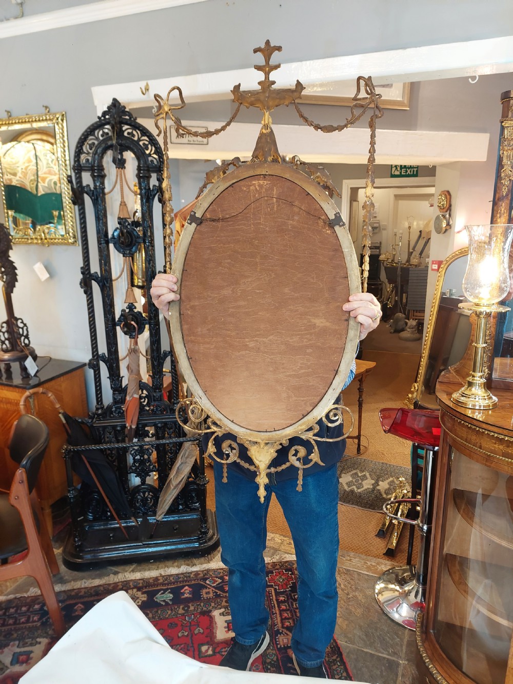 A late Victorian Adam Revival giltwood oval wall mirror decorated with an urn cresting, trailing ribbon swags, and scrollwork accents. View XIII