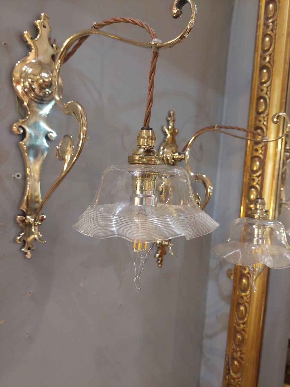 A pair of polished brass Art Nouveau wall sconces featuring decorative backplates, gooseneck arms, twisted flex, and ruffled clear glass shades. View III