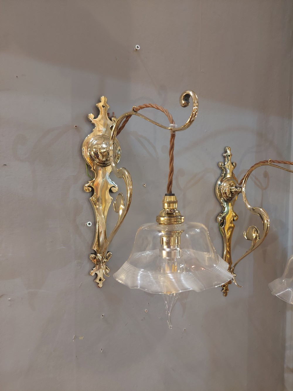 A pair of polished brass Art Nouveau wall sconces featuring decorative backplates, gooseneck arms, twisted flex, and ruffled clear glass shades. View IV