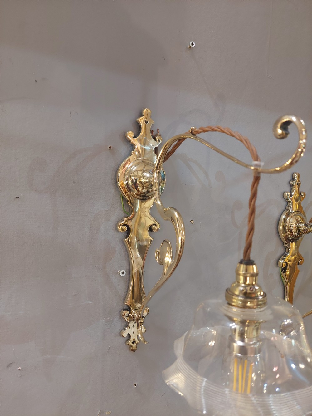 A pair of polished brass Art Nouveau wall sconces featuring decorative backplates, gooseneck arms, twisted flex, and ruffled clear glass shades. View V