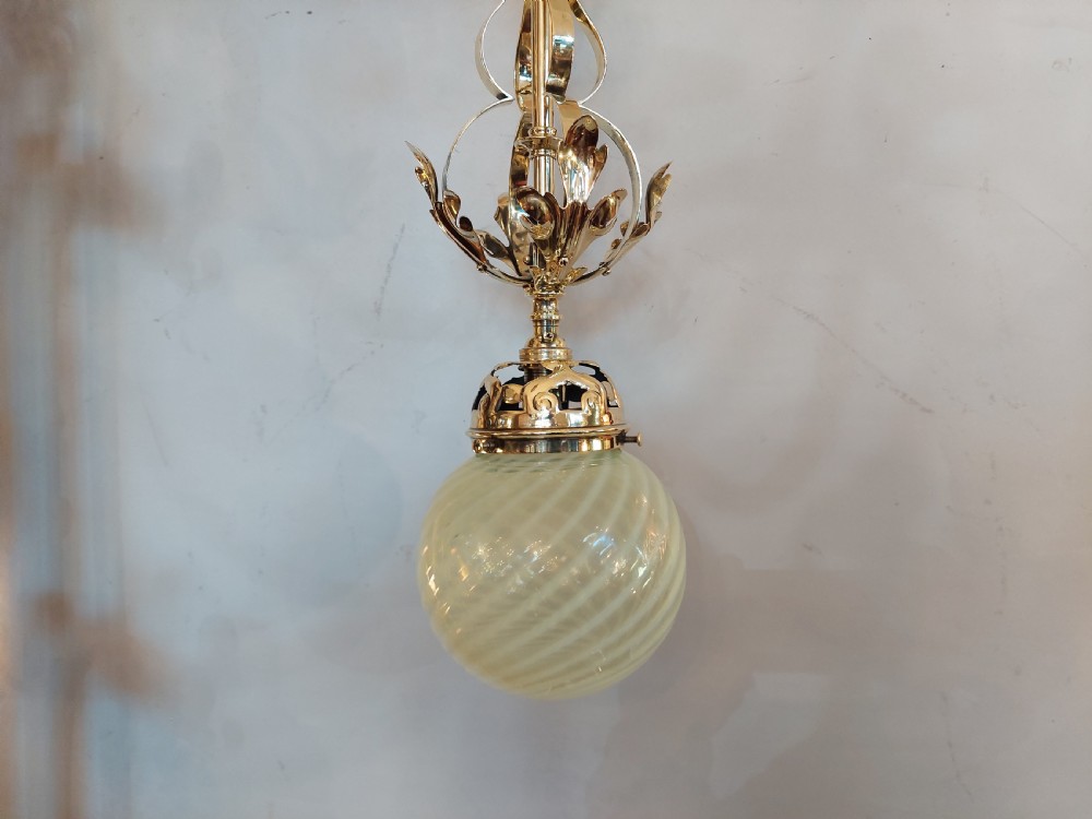 An Art Nouveau ceiling pendant light featuring polished brass scrollwork and leaf detailing suspending a swirled pale green glass globe shade. View III