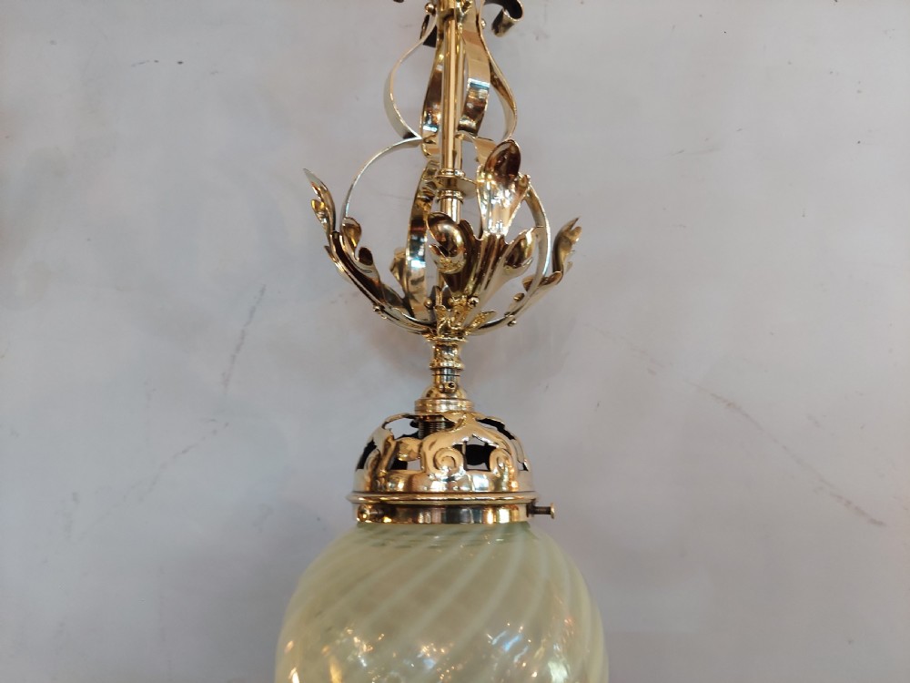 An Art Nouveau ceiling pendant light featuring polished brass scrollwork and leaf detailing suspending a swirled pale green glass globe shade. View IV