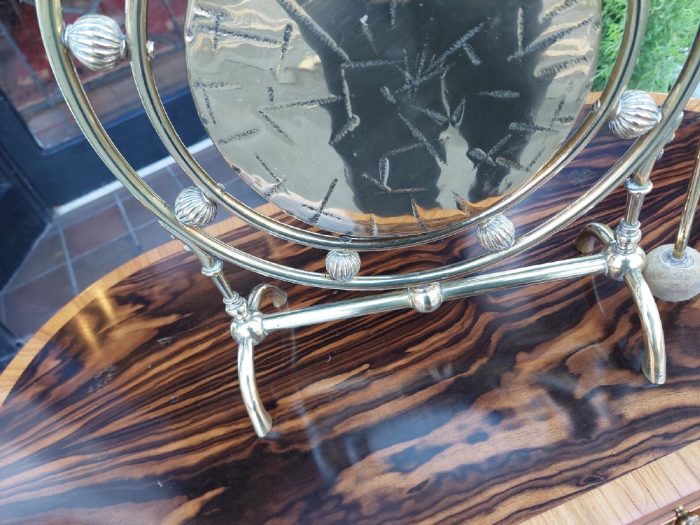A late 19th-century polished metal tabletop gong with a circular hammered centre plate, ribbed decorative beads, a framed stand, and an attached hanging striker. View II