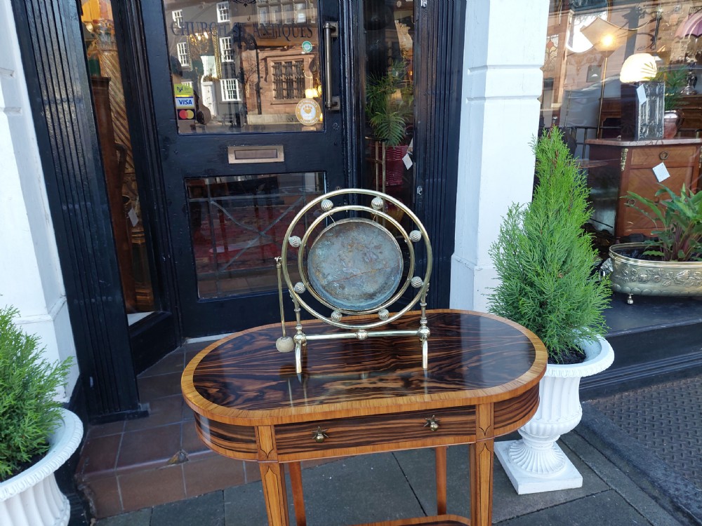 A late 19th-century polished metal tabletop gong with a circular hammered centre plate, ribbed decorative beads, a framed stand, and an attached hanging striker. View V