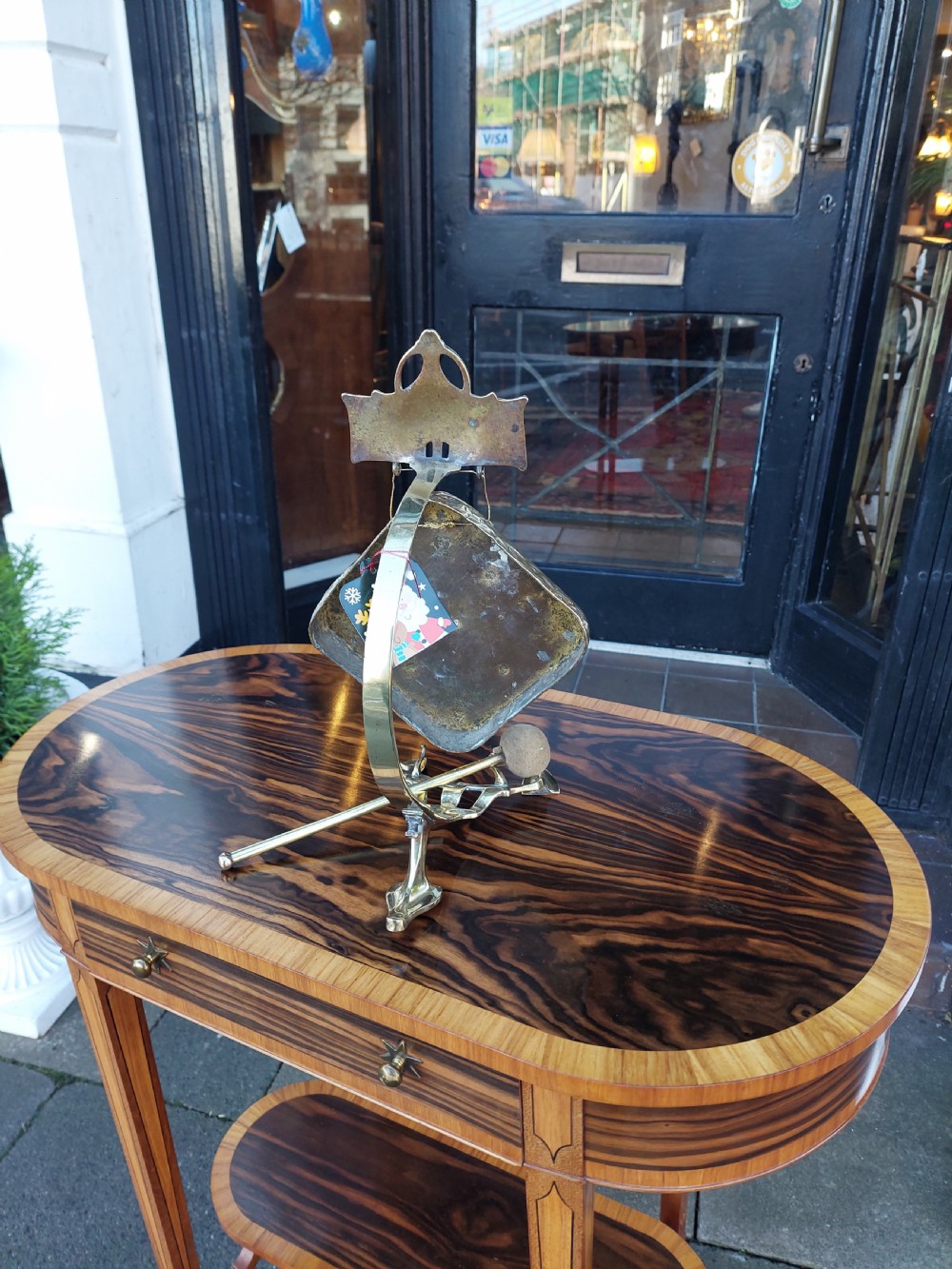 An Art Nouveau silver-plated table gong featuring a diamond-shaped suspended plate, stylized arched metal frame, and a mallet resting on a dual-pronged base. View VI