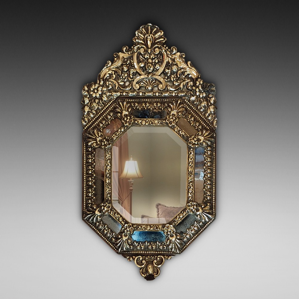 An antique Victorian octagonal cushion mirror featuring an embossed brass frame with floral cresting and mirrored border sections.