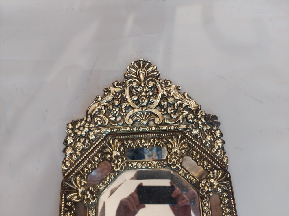 An antique Victorian octagonal cushion mirror featuring an embossed brass frame with floral cresting and mirrored border sections. View V