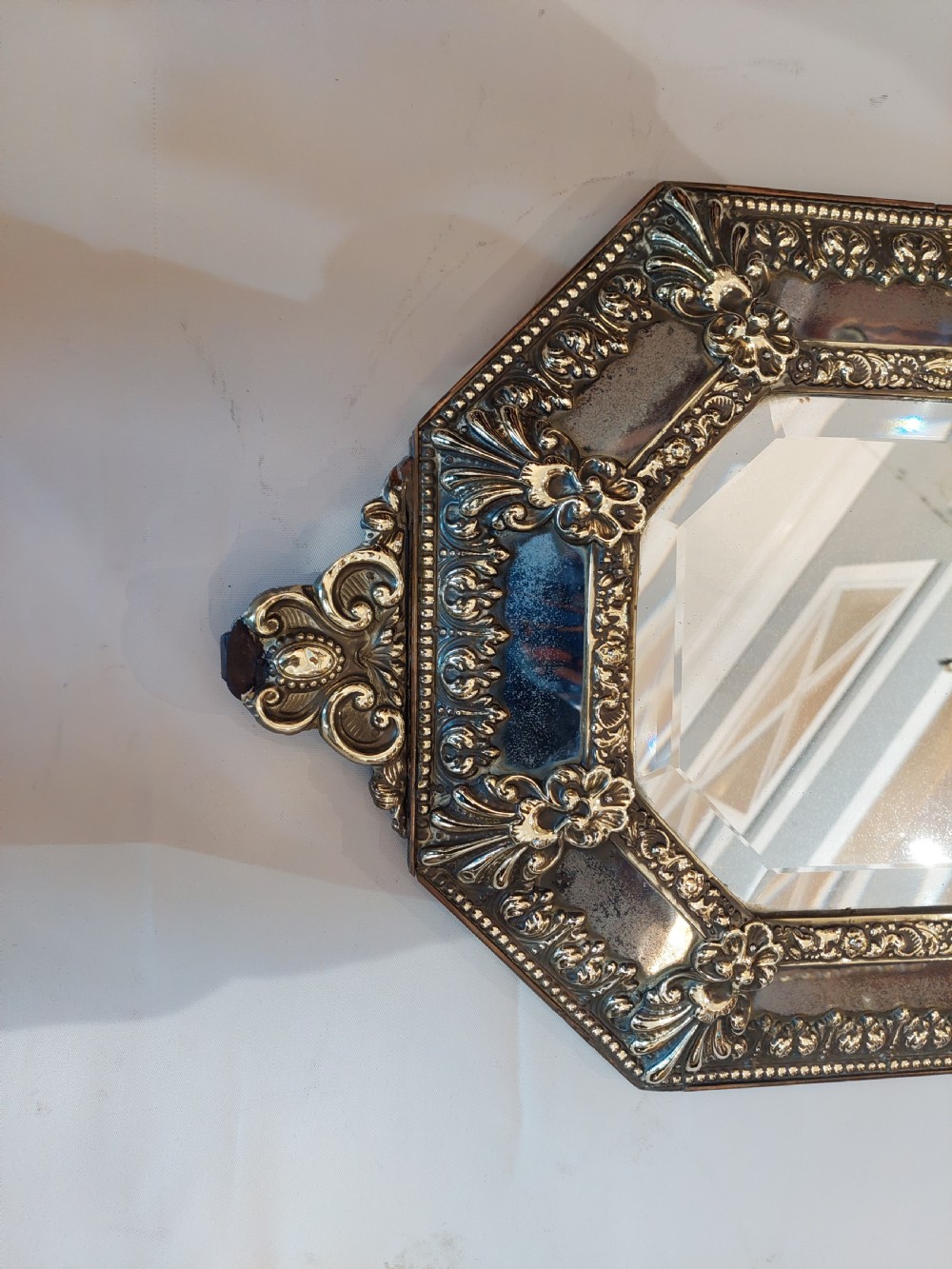 An antique Victorian octagonal cushion mirror featuring an embossed brass frame with floral cresting and mirrored border sections. View VII