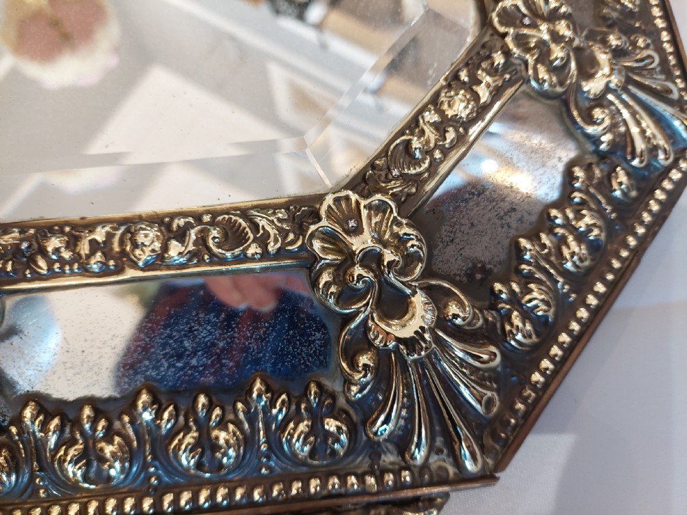 An antique Victorian octagonal cushion mirror featuring an embossed brass frame with floral cresting and mirrored border sections. View VIII