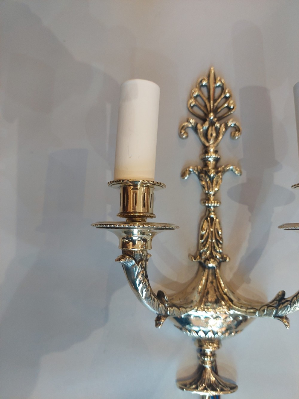 A set of four early 20th-century gilt brass twin-arm wall sconces featuring Neoclassical urn and anthemion motifs. View V