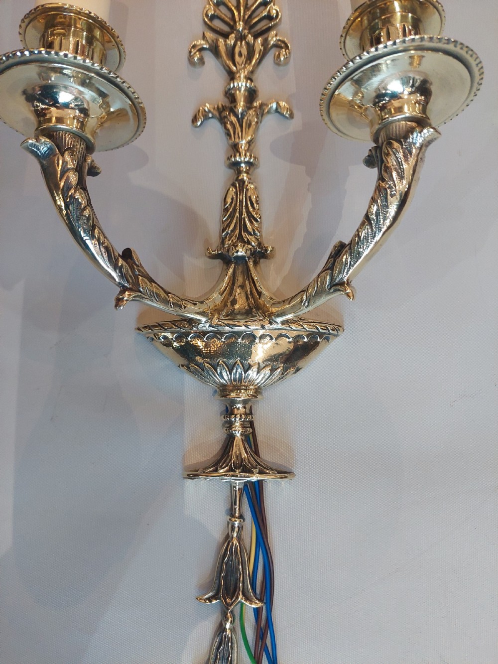 A set of four early 20th-century gilt brass twin-arm wall sconces featuring Neoclassical urn and anthemion motifs. View VI