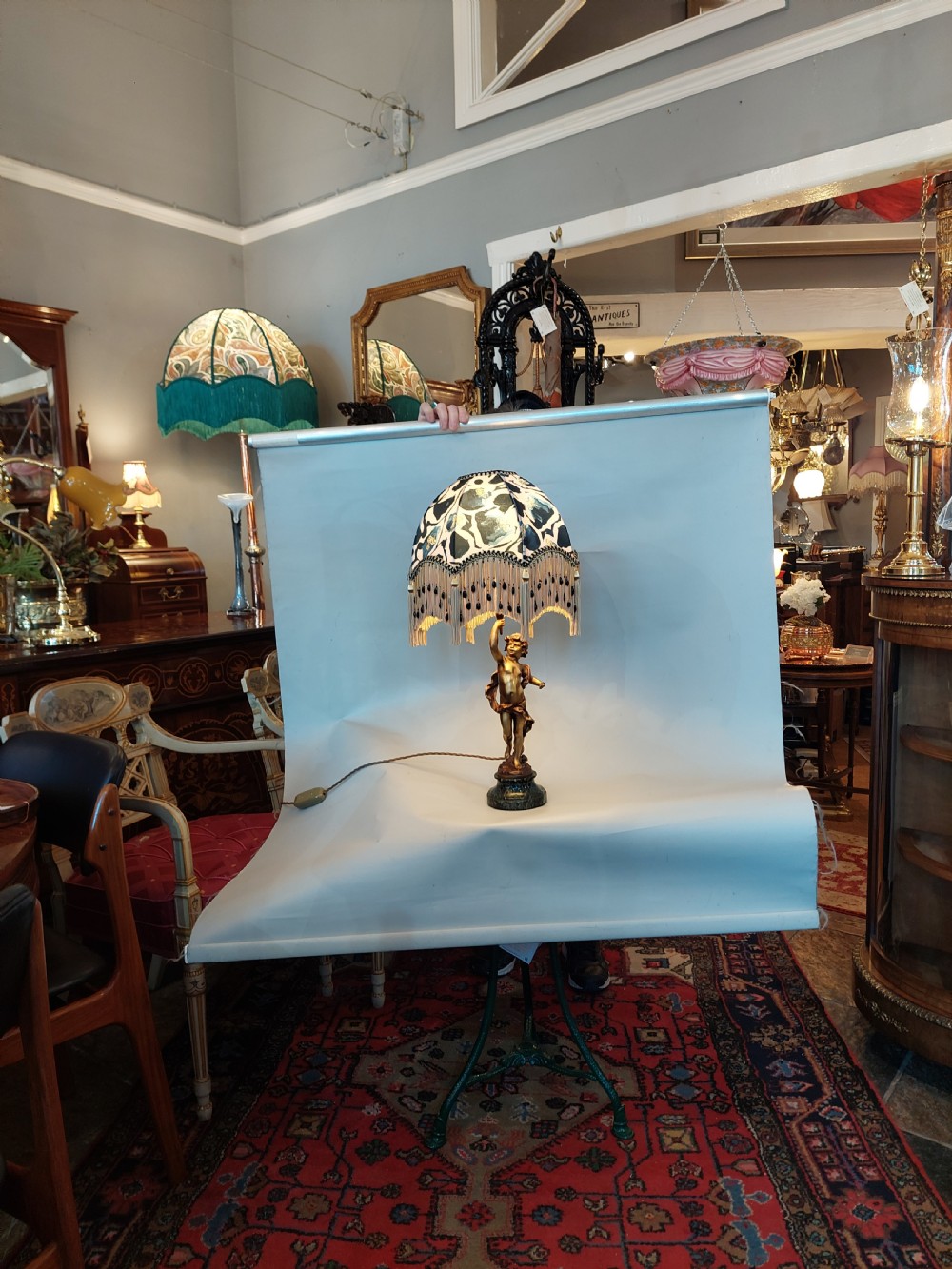 A cast bronze cherub statuette holding aloft a dome-shaped lampshade with patterned fabric and beaded tassel fringe, set on a dark marble base. View II